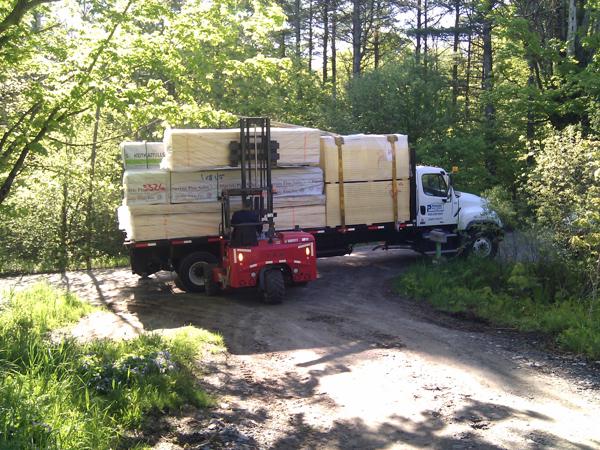 Truck with first load of wood being unloaded. The driver couldn't get the truck up the driveway, so he used his little forklift to haul the wood up to the house site.