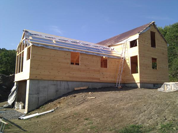 The one story section partially roofed.  From top down, you can see the first four layers: sheathing, Typar, foam, and strapping.  The next step is installing the metal roofing, which hasn't arrived yet.  The two story section is also waiting for metal roofing.