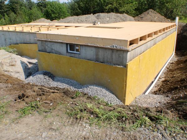 Foundation partially backfilled with stone. Still visible are the fiberglass drainage board and perimeter pipes.